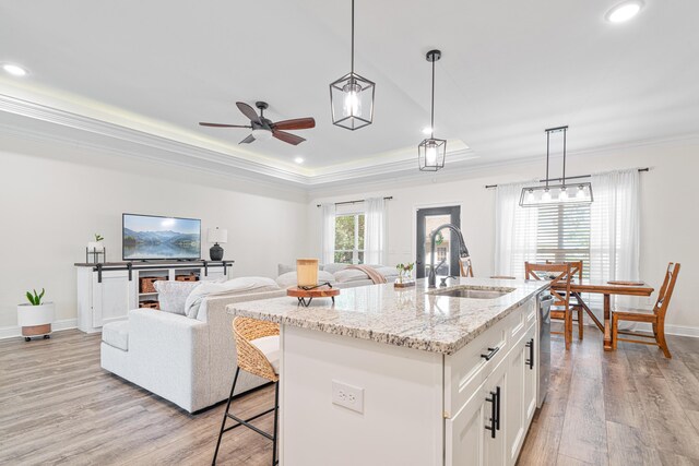 kitchen with light wood-style flooring, a sink, a tray ceiling, white cabinets, and crown molding