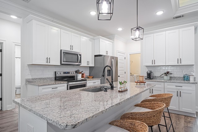 kitchen featuring wood finished floors, a breakfast bar, a sink, appliances with stainless steel finishes, and crown molding