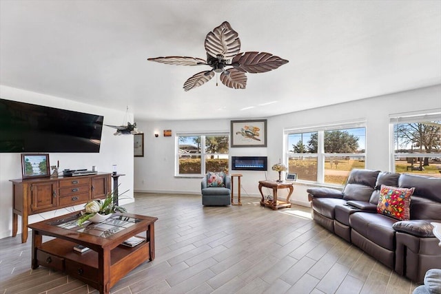 living area featuring ceiling fan, baseboards, a glass covered fireplace, and light wood-style floors