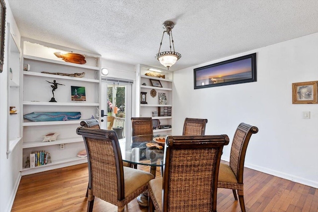 dining area with wood-type flooring, built in shelves, baseboards, and a textured ceiling