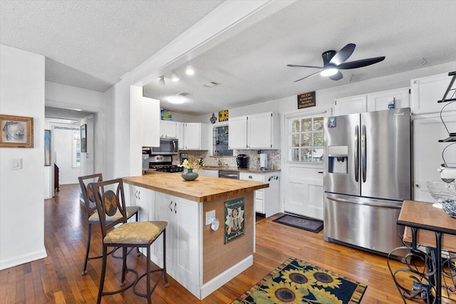 kitchen with dark wood finished floors, butcher block counters, appliances with stainless steel finishes, a kitchen bar, and white cabinetry