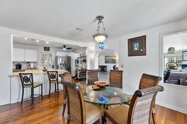 dining space with visible vents, arched walkways, a ceiling fan, dark wood-style floors, and a textured ceiling