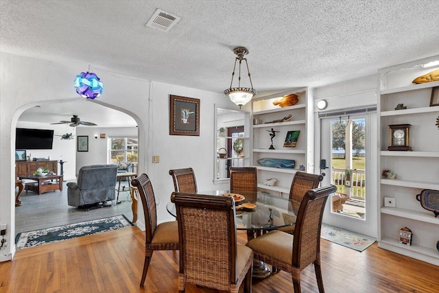 dining room with built in features, visible vents, arched walkways, hardwood / wood-style floors, and a textured ceiling