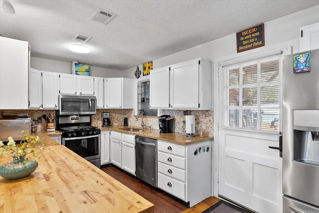 kitchen with visible vents, decorative backsplash, stainless steel appliances, white cabinetry, and a sink