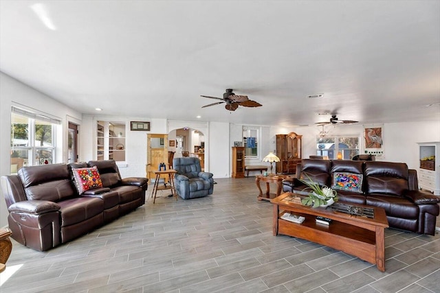 living area with a ceiling fan, arched walkways, visible vents, and wood tiled floor