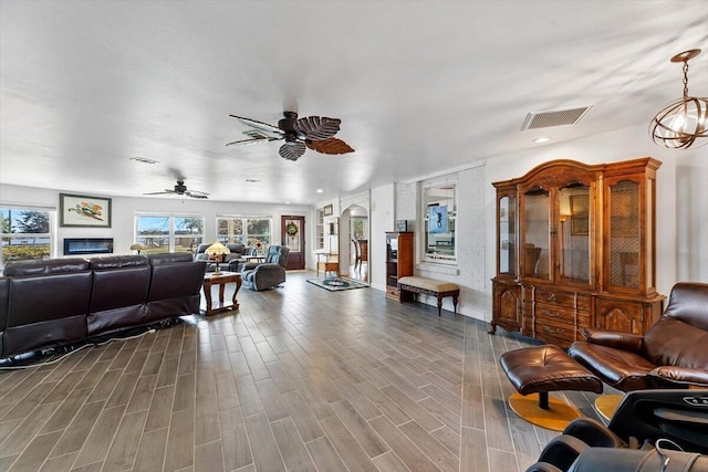 living room with ceiling fan with notable chandelier, visible vents, a glass covered fireplace, and wood finished floors