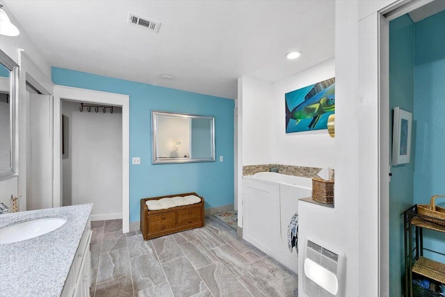 full bathroom featuring heating unit, visible vents, vanity, a tub, and baseboards