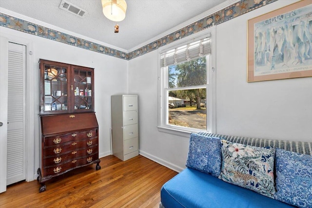 living area featuring visible vents, ornamental molding, a textured ceiling, wood finished floors, and baseboards