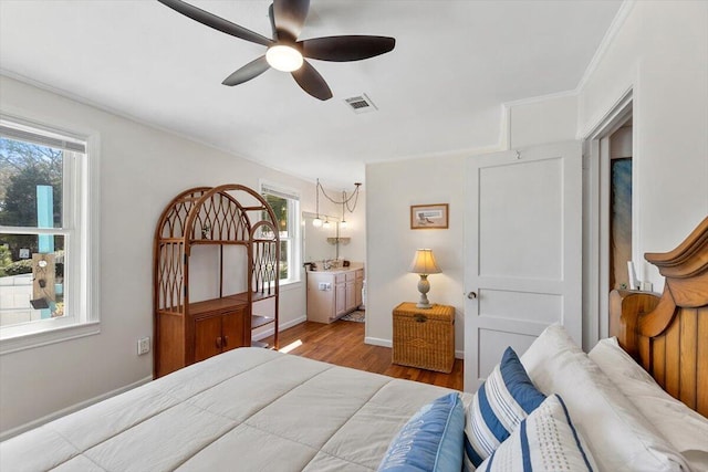 bedroom with ensuite bathroom, wood finished floors, visible vents, baseboards, and crown molding