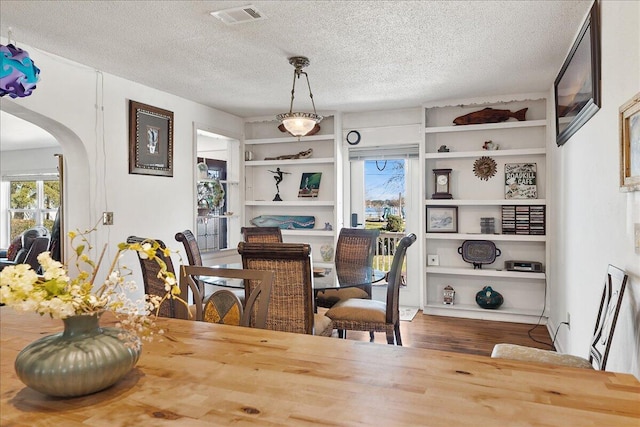 dining room featuring built in features, visible vents, arched walkways, wood finished floors, and a textured ceiling