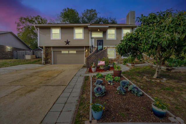 split foyer home featuring a vegetable garden, a chimney, concrete driveway, an attached garage, and fence