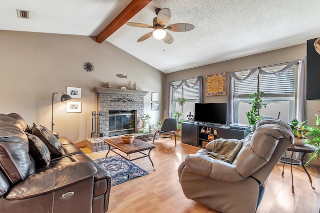 living room with vaulted ceiling with beams, visible vents, a brick fireplace, a textured ceiling, and wood finished floors