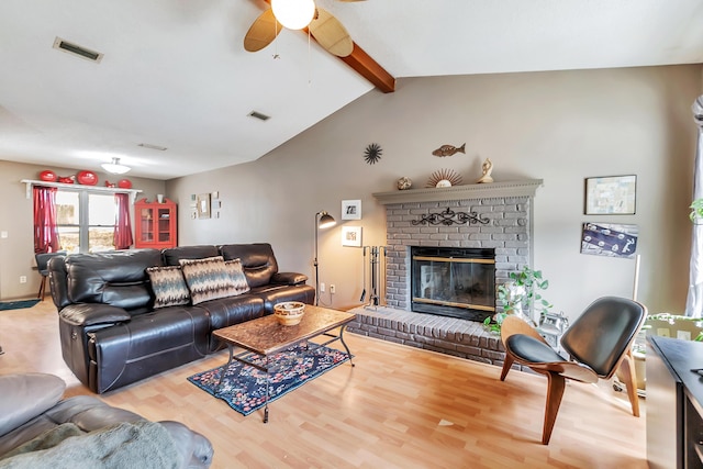 living room featuring lofted ceiling with beams, a brick fireplace, wood finished floors, and visible vents