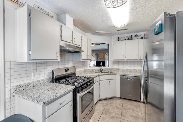 kitchen featuring light tile patterned floors, appliances with stainless steel finishes, white cabinets, a sink, and under cabinet range hood