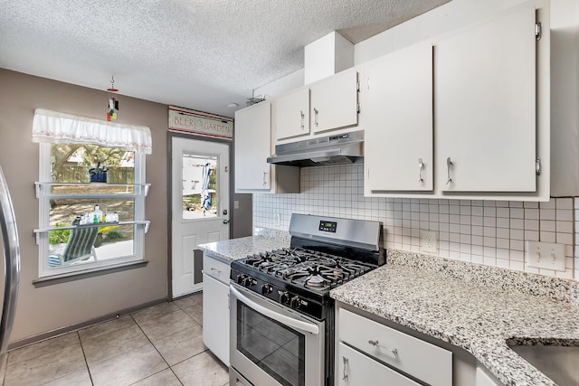 kitchen featuring light tile patterned flooring, under cabinet range hood, white cabinetry, stainless steel gas range, and backsplash