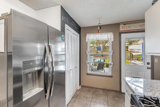 kitchen with light tile patterned floors, a textured ceiling, stainless steel refrigerator with ice dispenser, light stone countertops, and range with gas cooktop