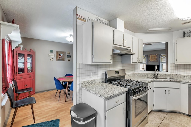 kitchen with stainless steel appliances, decorative backsplash, a sink, a textured ceiling, and under cabinet range hood