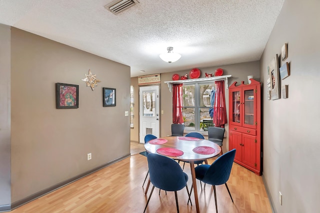 dining area with light wood-style floors, visible vents, a textured ceiling, and baseboards