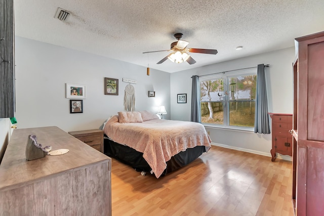 bedroom with a textured ceiling, light wood-type flooring, visible vents, and a ceiling fan