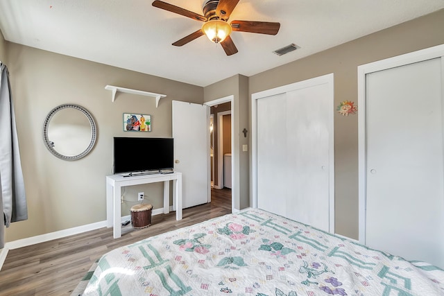 bedroom with two closets, visible vents, a ceiling fan, wood finished floors, and baseboards