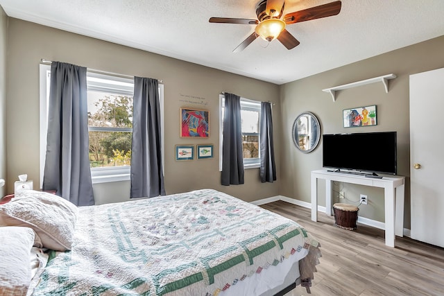 bedroom with multiple windows, a textured ceiling, baseboards, and wood finished floors