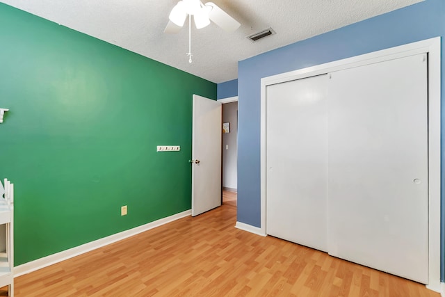 unfurnished bedroom with a textured ceiling, wood finished floors, visible vents, baseboards, and a closet