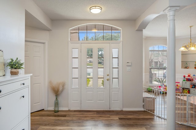 foyer featuring dark hardwood / wood-style floors, a chandelier, a textured ceiling, and ornate columns