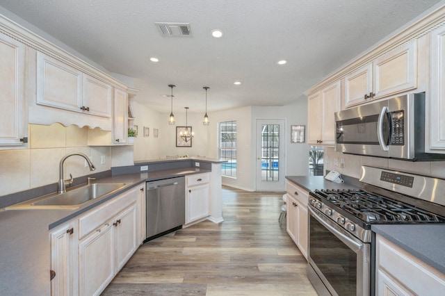 kitchen with appliances with stainless steel finishes, sink, decorative backsplash, hanging light fixtures, and light wood-type flooring