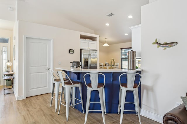 kitchen with visible vents, light wood-style floors, white cabinetry, stainless steel fridge, and a kitchen breakfast bar