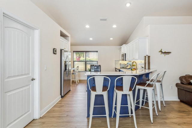 kitchen featuring appliances with stainless steel finishes, white cabinets, light wood-style floors, and decorative backsplash