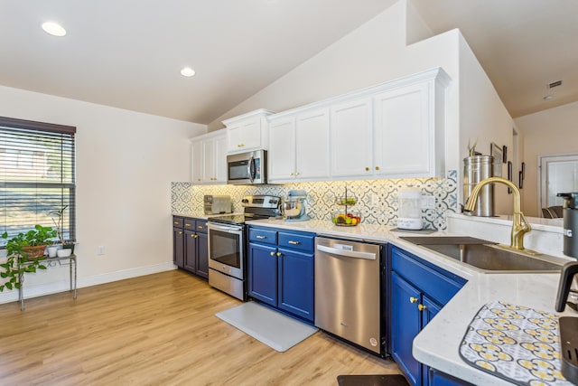 kitchen featuring blue cabinetry, appliances with stainless steel finishes, white cabinetry, vaulted ceiling, and a sink