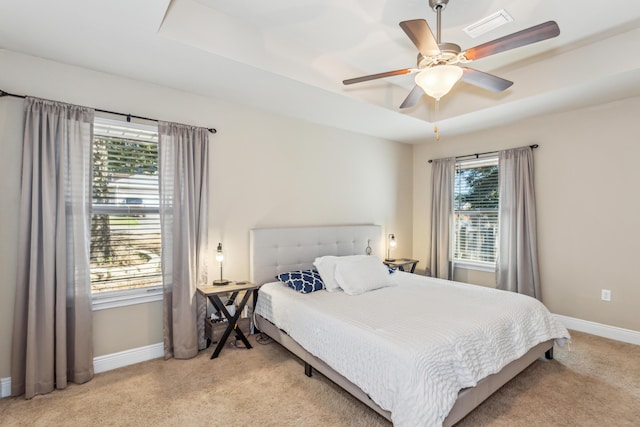 carpeted bedroom with a ceiling fan, visible vents, a tray ceiling, and baseboards