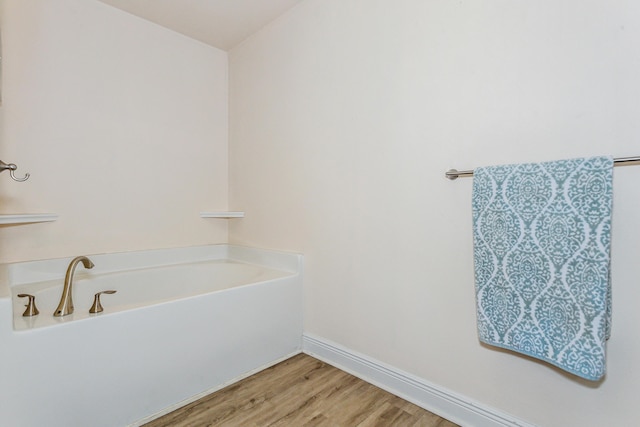 bathroom with wood finished floors, a bath, and baseboards