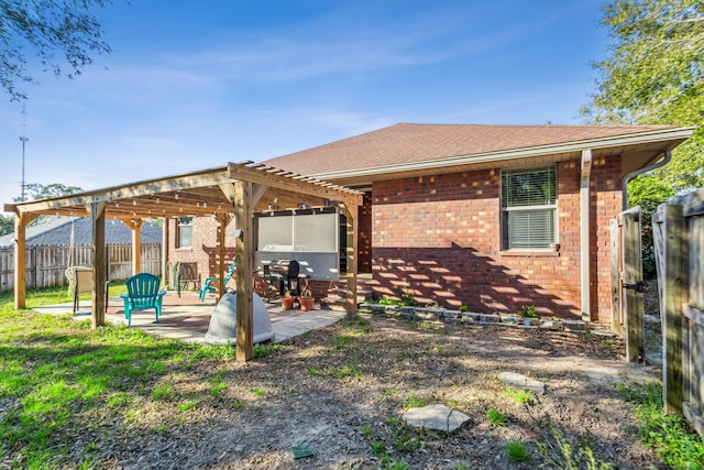 rear view of property featuring roof with shingles, brick siding, a patio area, fence, and a pergola