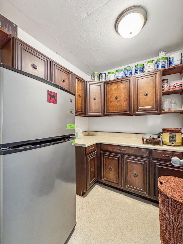 kitchen featuring dark brown cabinetry, stainless steel fridge, and a textured ceiling