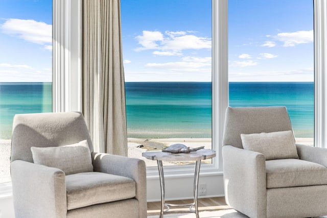 living area with a water view, hardwood / wood-style floors, and a view of the beach