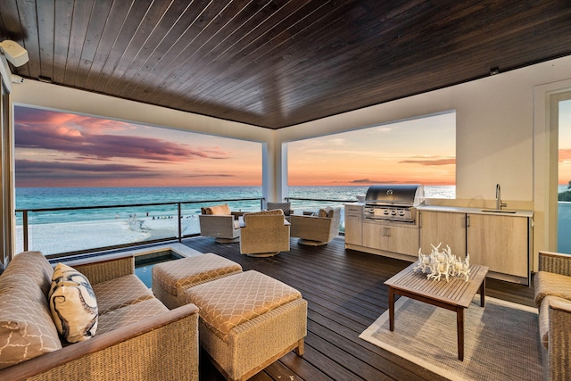 deck at dusk featuring exterior kitchen, a water view, a beach view, and grilling area