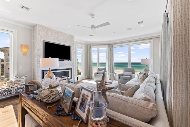 living room featuring wood-type flooring, ornamental molding, ceiling fan, and a fireplace