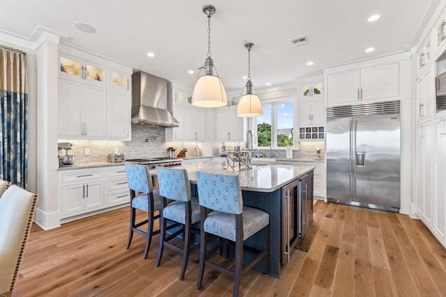 kitchen with white cabinets, stainless steel built in refrigerator, a kitchen island, and wall chimney range hood