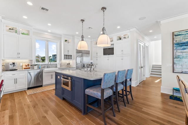 kitchen with decorative light fixtures, a breakfast bar area, white cabinets, a kitchen island with sink, and stainless steel appliances