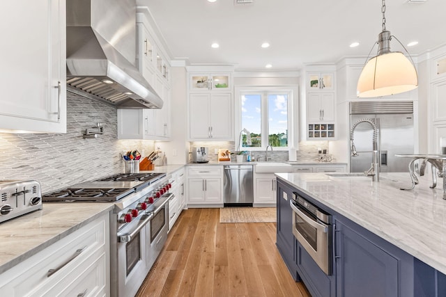 kitchen featuring white cabinetry, hanging light fixtures, high quality appliances, light stone countertops, and wall chimney range hood