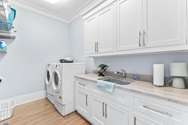 laundry area featuring sink, cabinets, washing machine and clothes dryer, crown molding, and light hardwood / wood-style flooring