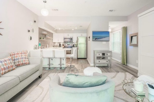 living area featuring light wood finished floors, visible vents, and baseboards