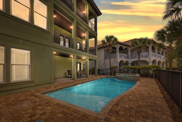 pool at dusk with a patio area and an in ground hot tub