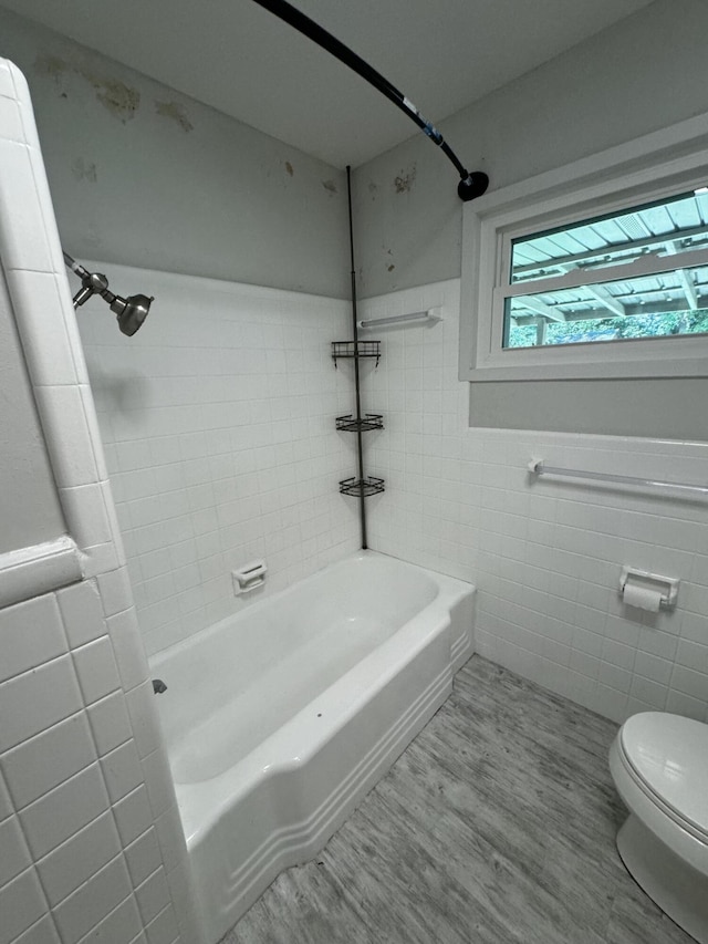 bathroom with hardwood / wood-style flooring, tiled shower / bath, tile walls, and toilet