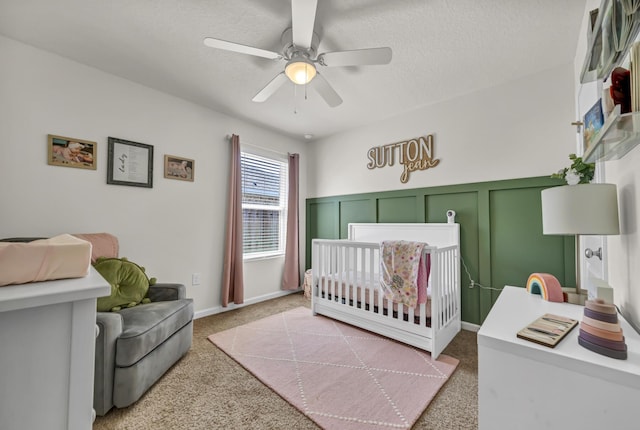 bedroom featuring light colored carpet, a decorative wall, ceiling fan, a textured ceiling, and a nursery area