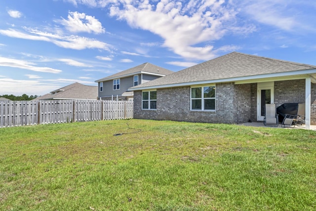 rear view of house featuring brick siding, roof with shingles, fence, and a yard