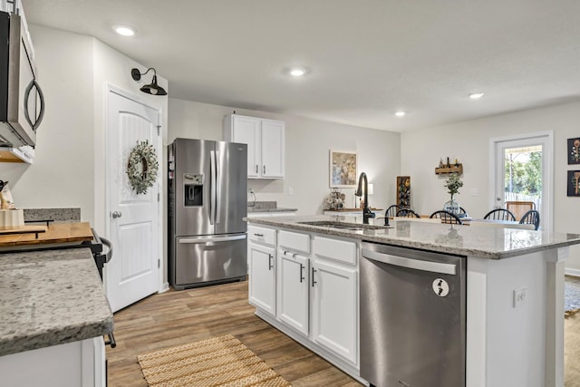 kitchen featuring appliances with stainless steel finishes, a kitchen island with sink, light wood-style floors, white cabinetry, and a sink