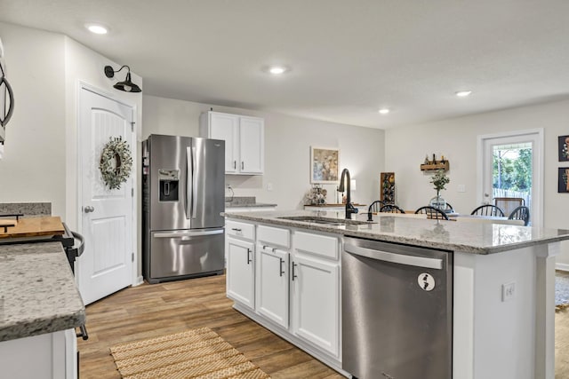 kitchen with light wood-style flooring, stainless steel appliances, a sink, white cabinets, and an island with sink