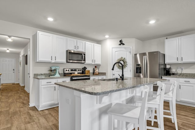 kitchen featuring a sink, white cabinetry, a kitchen breakfast bar, appliances with stainless steel finishes, and light wood finished floors